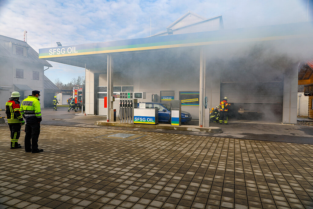 Eine brennende, rauchende Tankstelle, in der Feuerwehrmänner löschen