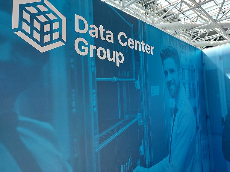 Wand, auf der Data Center Group und das Logo der DCG zu sehen ist und ein Mann, in blau