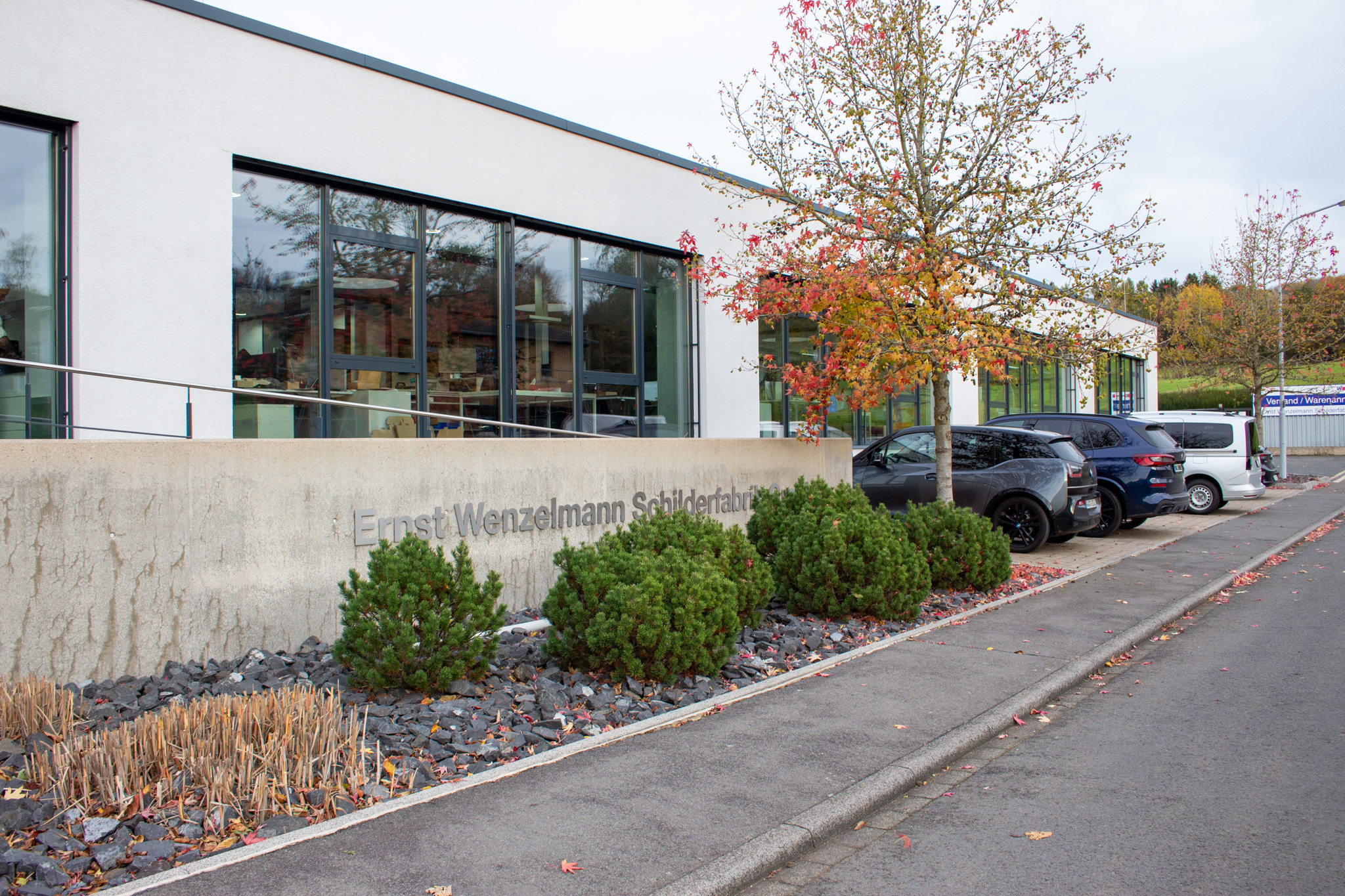 Company building of the Wenzelmann sign factory with bushes and cars in the foreground