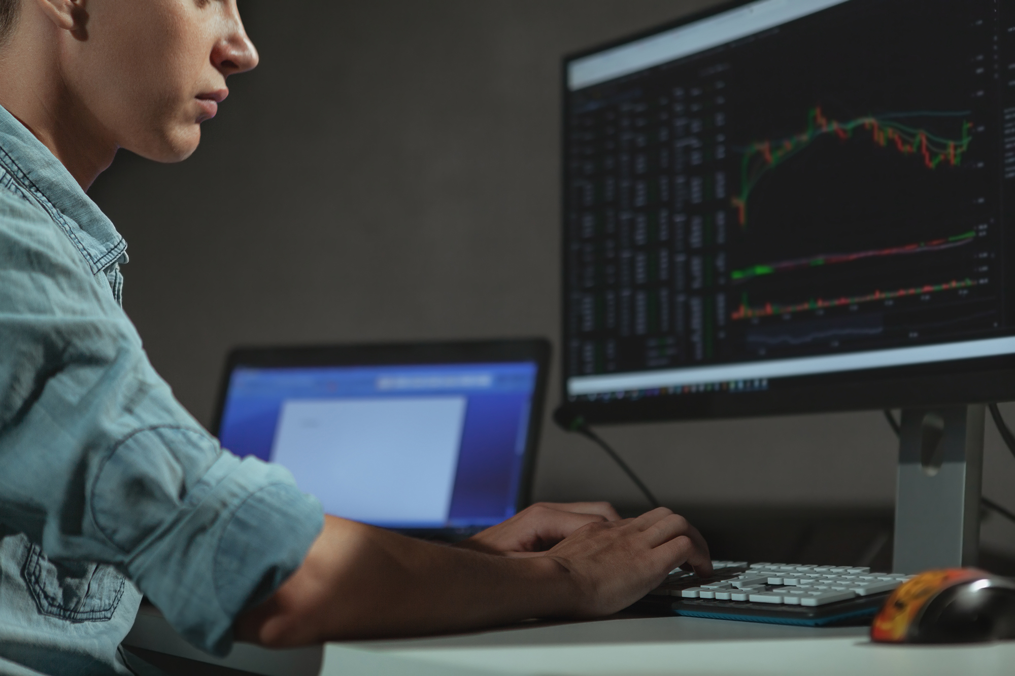 Man at a desk analyzing data on a screen, left a laptop